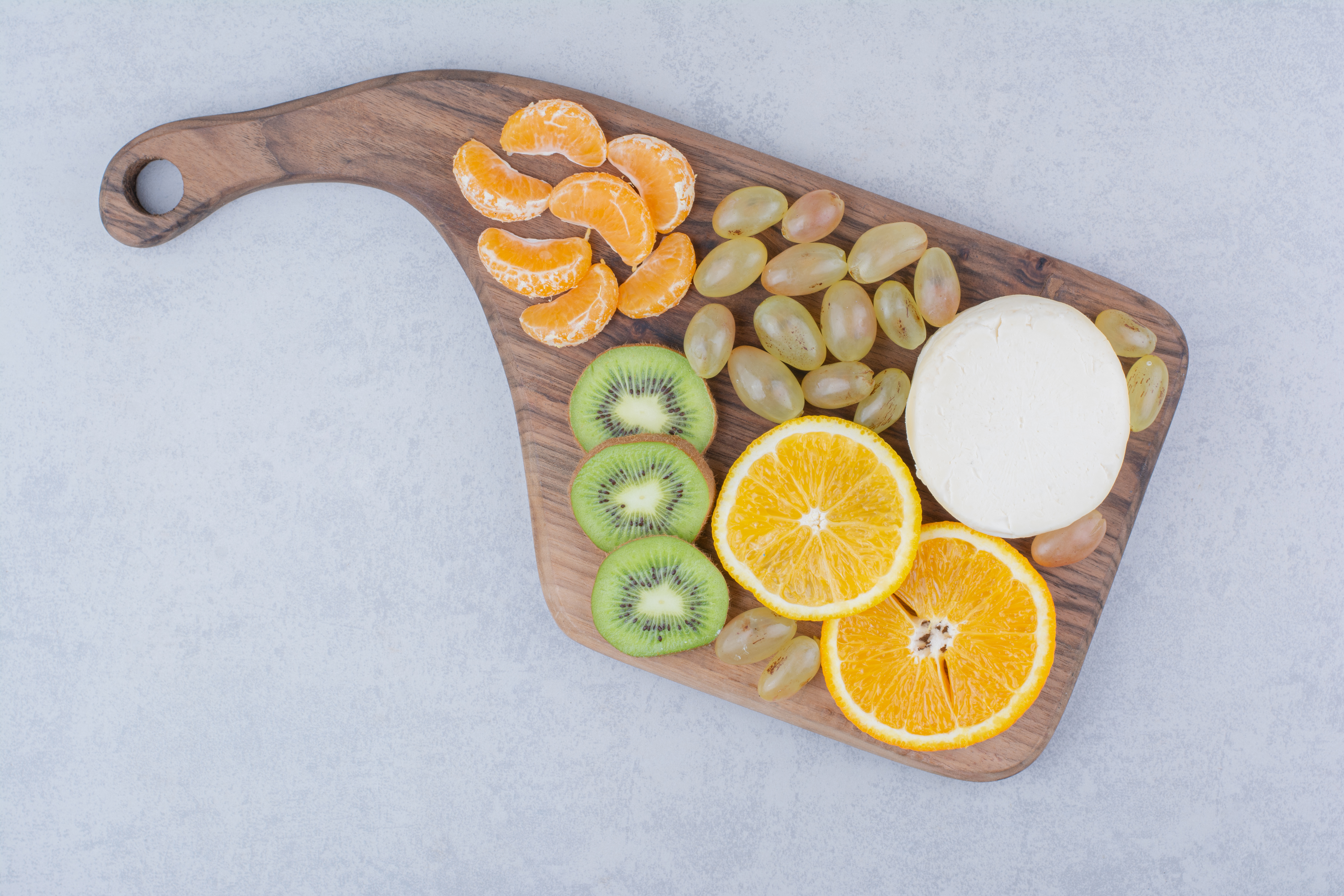 A wooden cutting board with whole cheese and sliced fruits